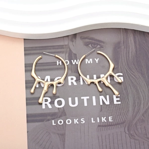 Minimalist golden liquid lava drop earrings on an artistic magazine and wave plate background
