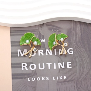 Ginkgo leaf earrings with green enamel and faux pearl on a lifestyle magazine backdrop