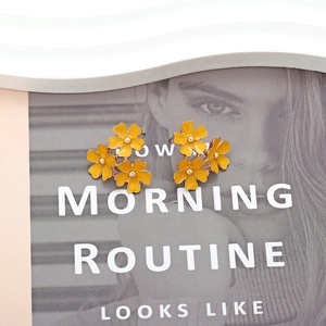 Elegant yellow enamel flower stud earrings with gold center on a lifestyle magazine background