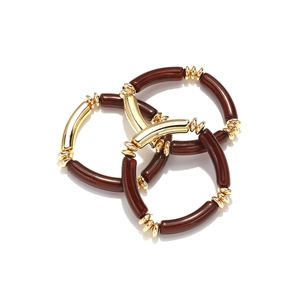Three-piece set of amber resin and gold metal beaded stretch bracelets on white background