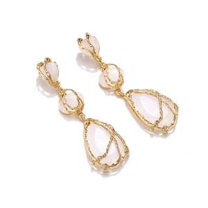 Détail de boucles d'oreilles pendantes dorées avec métal texturé et résine laiteuse