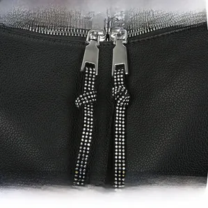 Close-up of black lychee leather handbag featuring silver zippers and rhinestone pulls