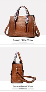 Detail of brown faux crocodile leather handbag with silk scarf on handle and gold hardware