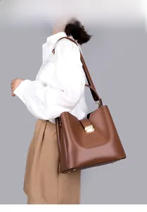 Vue latérale du sac seau en cuir marron foncé avec fermoir doré porté par un modèle