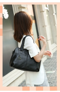 Detail of black leather shoulder bag with FASHION metal pendant and pebble grain texture