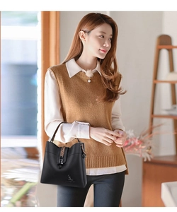 Close-up of black leather bucket bag with kangaroo logo carried by model in casual outfit