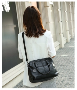 Rear view of model holding a black leather tote bag with dual handles and metal charm