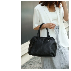 Detail of black textured leather tote bag with silver rivets and metal letter charm