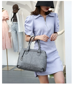 Detail of grey textured leather handbag with dual handles and metal rings on a dress