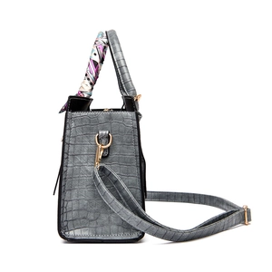 Grey crocodile pattern handbag with silk scarf handle and adjustable strap on white background