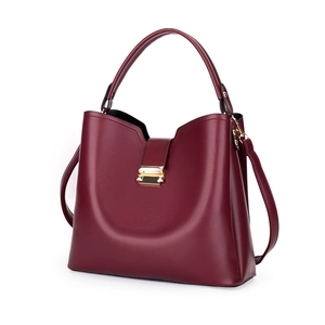 Sac seau minimaliste en cuir bordeaux avec fermoir doré et poignée sur fond blanc