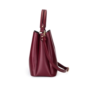 Sac seau minimaliste en cuir bordeaux avec poignée et finitions dorées sur fond blanc