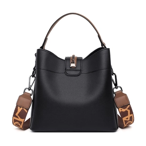 Minimalist black pebble leather bucket bag with brown handles and a patterned strap