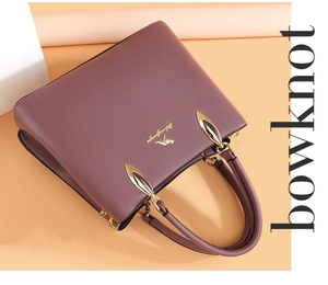 Détail du sac à main violet en cuir grainé avec logo kangourou doré et doubles poignées