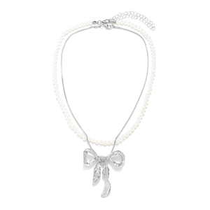 Double-layered pearl necklace with metallic bow pendant on minimalist white background