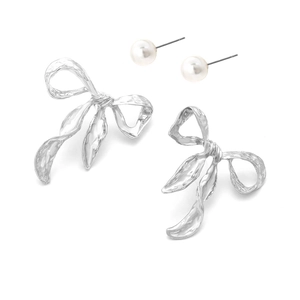 Detail view of silver bow-knot earrings with hammered texture and white pearl studs