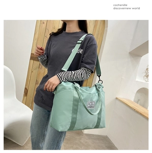 Mint green nylon travel bag shown on shoulder in a minimalist indoor setting