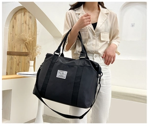 Close-up of black nylon travel tote with brand patch and adjustable shoulder strap attachment