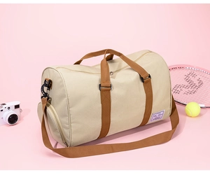 Detail view of large beige canvas travel bag featuring brown straps and branding patch