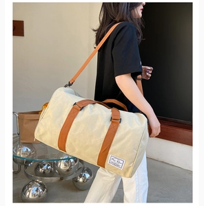 Detail of beige canvas travel bag with brown straps and brand label on a female model