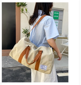 Detail of a large beige canvas travel bag with orange straps shown in a street setting