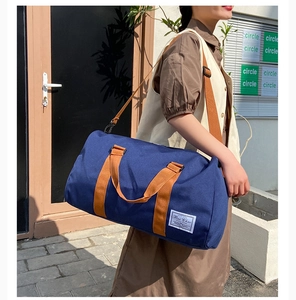 Detail of dark blue canvas travel bag with brown straps worn by a model in a street setting