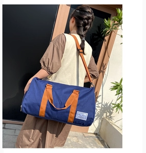 Rear view of a model carrying a large dark blue canvas duffel bag with brown straps