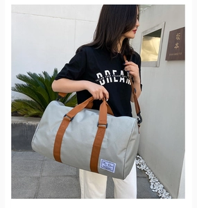 Close-up of a light grey canvas travel bag with brown straps and a branded woven label