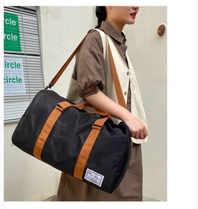 Close-up of black canvas travel bag featuring brown straps and woven brand label