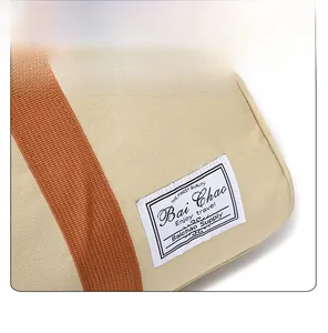 Close-up of beige canvas travel bag with orange strap and vintage fabric patch