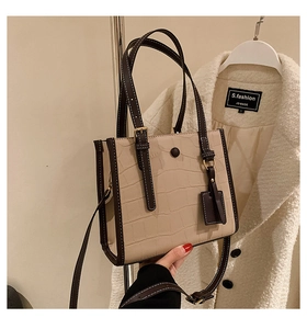 Detail of beige crocodile pattern tote bag with dark brown contrast handles and gold hardware