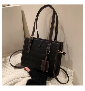 Detail of black crocodile texture tote bag with brown trim and gold hardware on soft rug