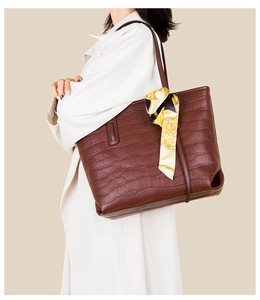 Detail of brown crocodile pattern tote bag with decorative scarf on shoulder strap