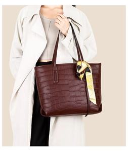 Detail of dark brown croc-pattern tote bag with decorative scarf on handle by model