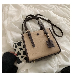 Detail of stone embossed pattern tote bag with polished golden bottom studs and dark brown handles