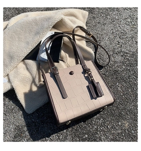 Detailed view of beige crocodile embossed tote bag with brown handles and metal studs