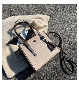 Close-up of beige crocodile embossed tote bag with brown trim on soft fabric
