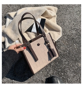 Close-up of beige crocodile pattern tote bag with brown trim on a stylish outdoor background