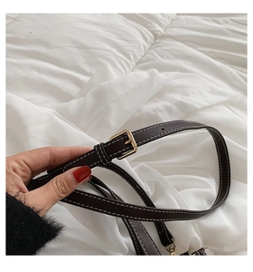 Detail of dark brown leather strap with white stitching and golden adjustable buckle