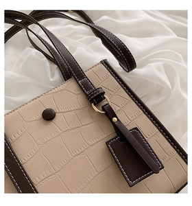 Macro detail of beige crocodile embossed tote bag with brown straps and gold ring hardware