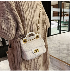 Détail d'un sac bandoulière en peluche blanche avec finitions dorées porté par un mannequin