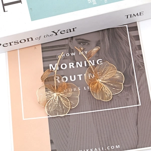Detailed view of woven metal leaf earrings in golden finish on art magazines