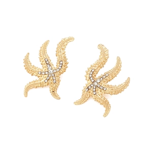 Macro detail of gold starfish earrings featuring intricate white rhinestone embellishments
