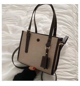 Detail of stone embossed pattern tote bag with contrast brown trim and golden metal hooks