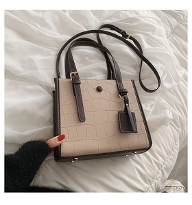 Detail of beige crocodile pattern tote with dark brown trim and bottom metal studs