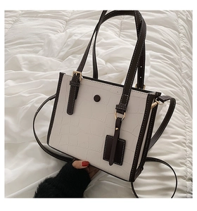 Detail of white crocodile embossed tote bag with black piping and adjustable shoulder strap