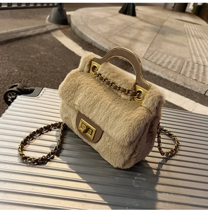 Détail d'un sac à main beige en fausse fourrure avec chaîne dorée et fermoir sur une valise