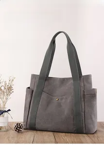 Dettaglio di una borsa tote in tela grigio scuro con rivetti su tavolo di legno