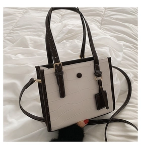 Detail of white crocodile pattern tote bag with brown handles and gold hardware on linen