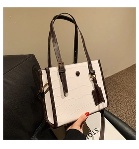 Detail of white crocodile embossed leather tote with contrasting brown straps and gold rivets